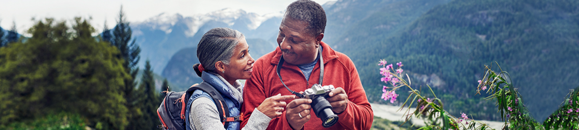 A mature African American couple looks at a camera against a mountain backdrop.