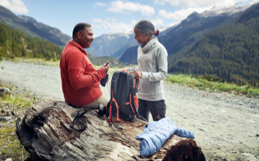 A couple shares a smile in front of mountain peaks covered in pine trees.