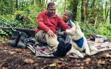 A couple sits in the woods, sharing a smile.