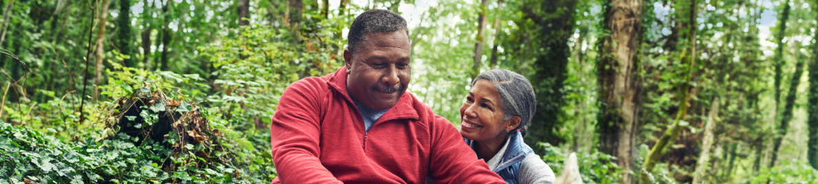 A couple sits in the woods, sharing a smile.