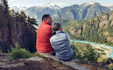 A couple sits on a bluff admiring a view of distant
                    mountains.