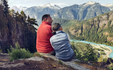 A couple sits on a bluff admiring a view of distant
                    mountains.