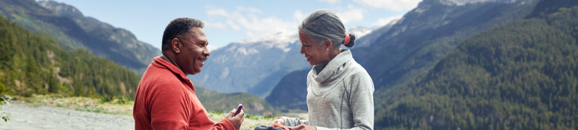 A couple shares a smile in front of mountain peaks covered in pine trees.